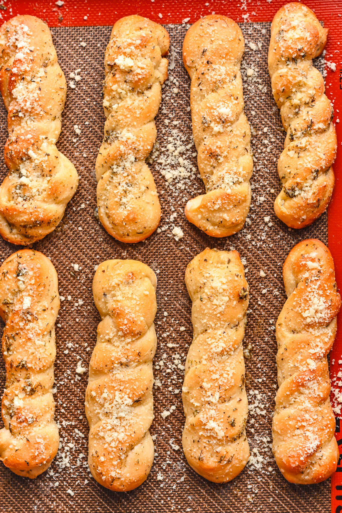 Eight breadsticks topped with parmesan on a baking sheet. 