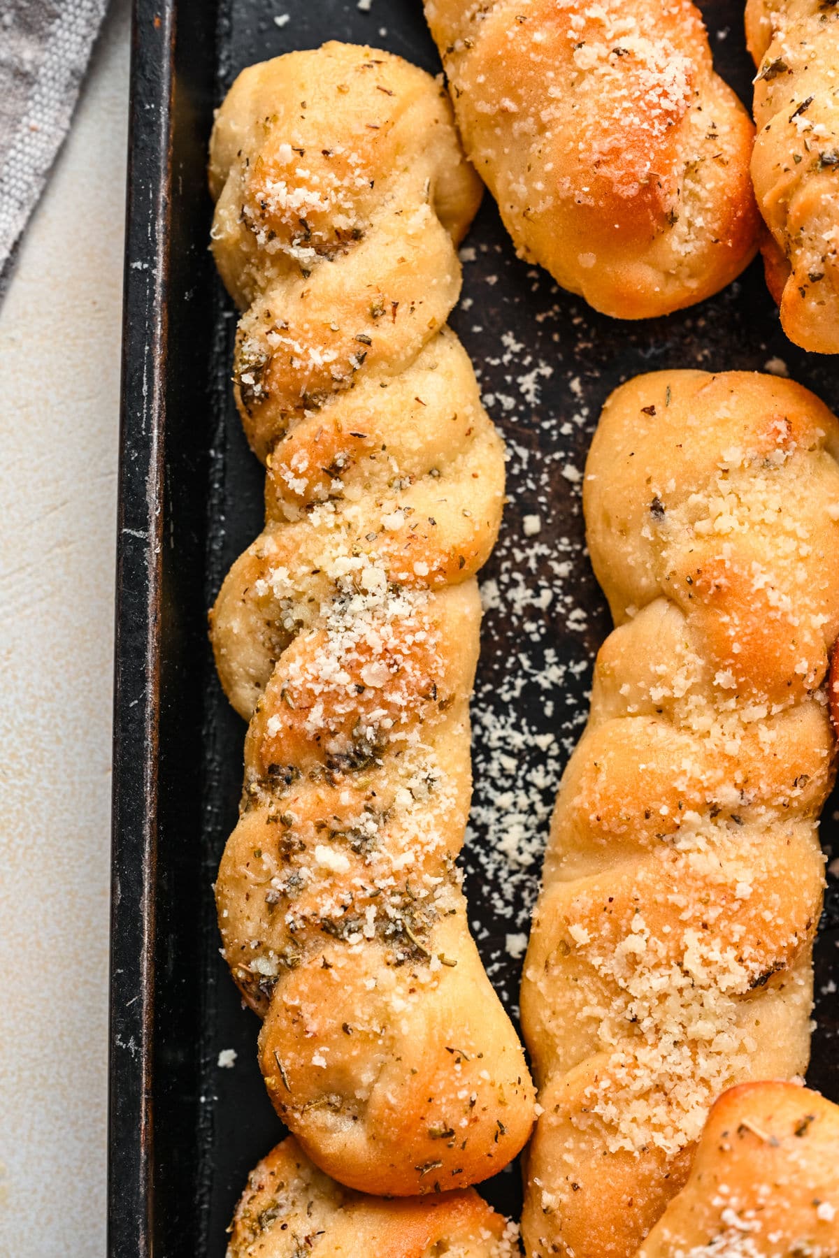 Closeup photo of a twisted breadstick on a dark baking pan.