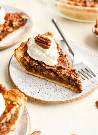 A slice of chocolate pecan pie topped with whipped cream and a pecan half.