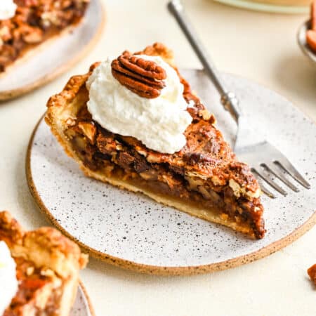 A slice of chocolate pecan pie topped with whipped cream and a pecan half.