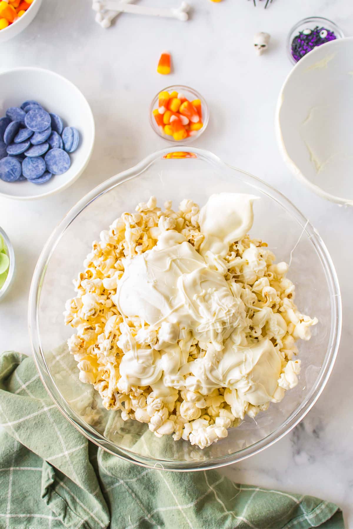 Popcorn and melted white chocolate in a glass mixing bowl. 