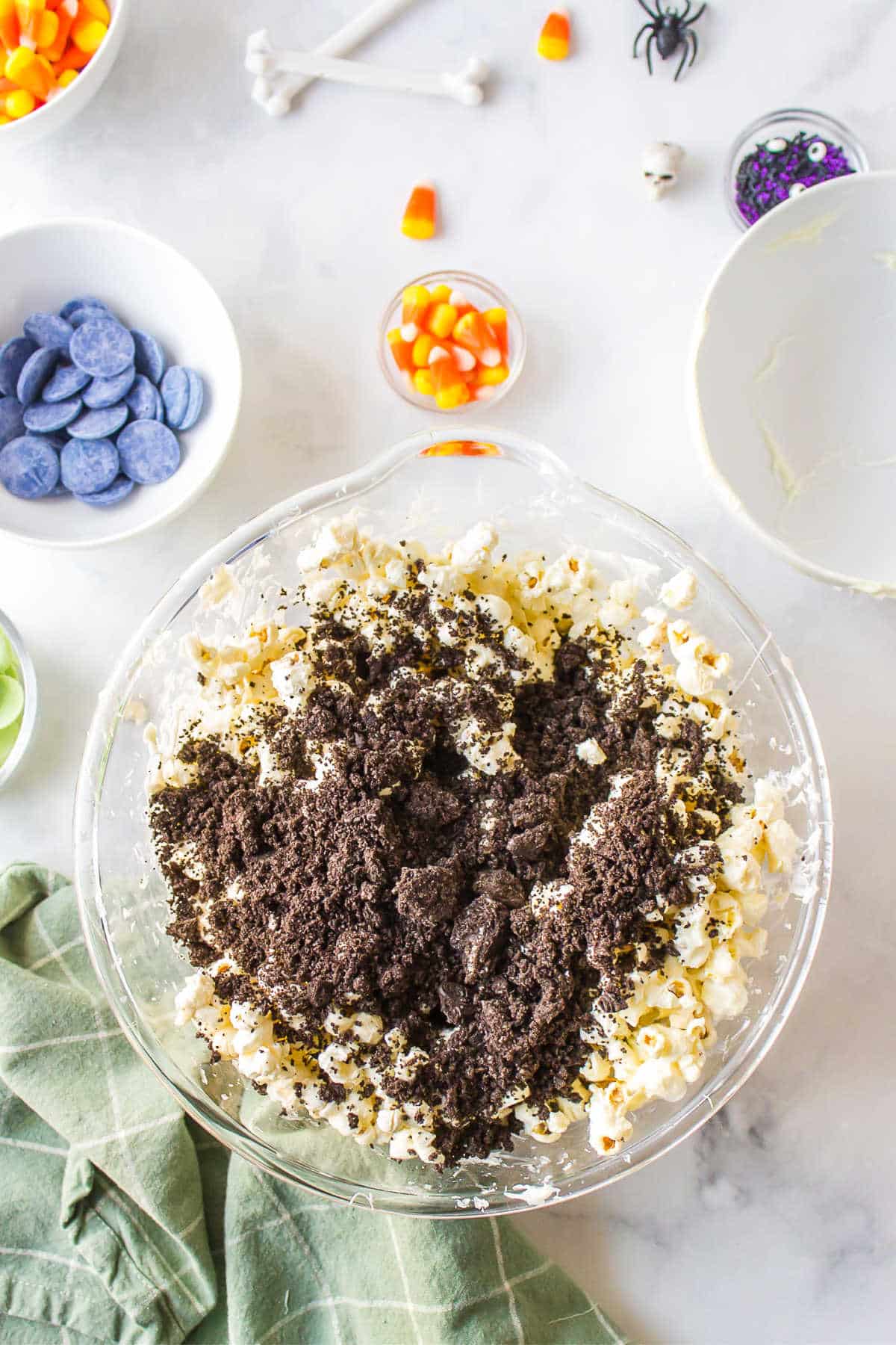 Oreo cookie crumbs on top of white chocolate popcorn mixture in a glass mixing bowl. 