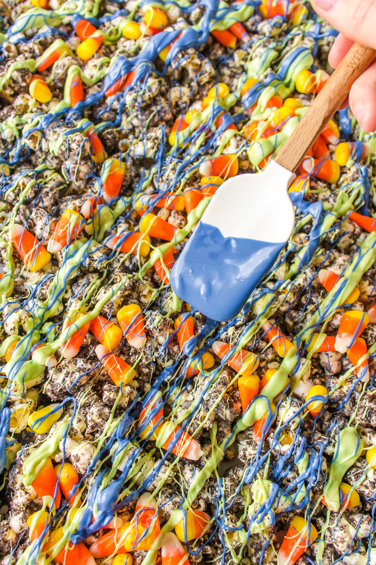 A rubber spatula drizzling candy melt over Halloween popcorn. 