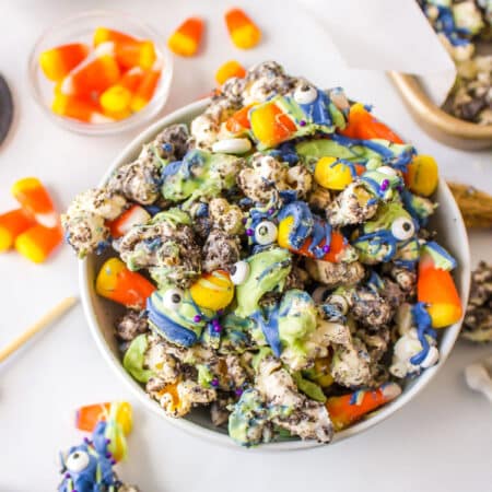 A white bowl of Halloween popcorn surrounded by candy corn and plastic spiders.