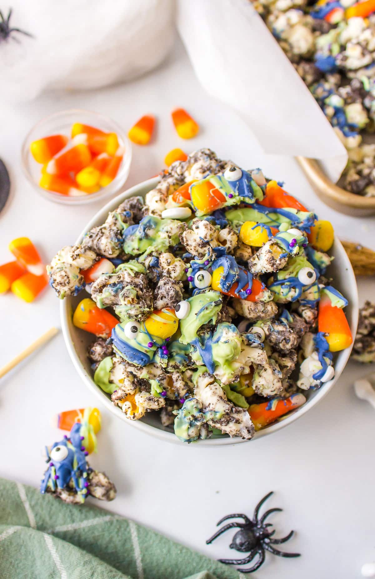 A white bowl of Halloween popcorn surrounded by candy corn and plastic spiders.