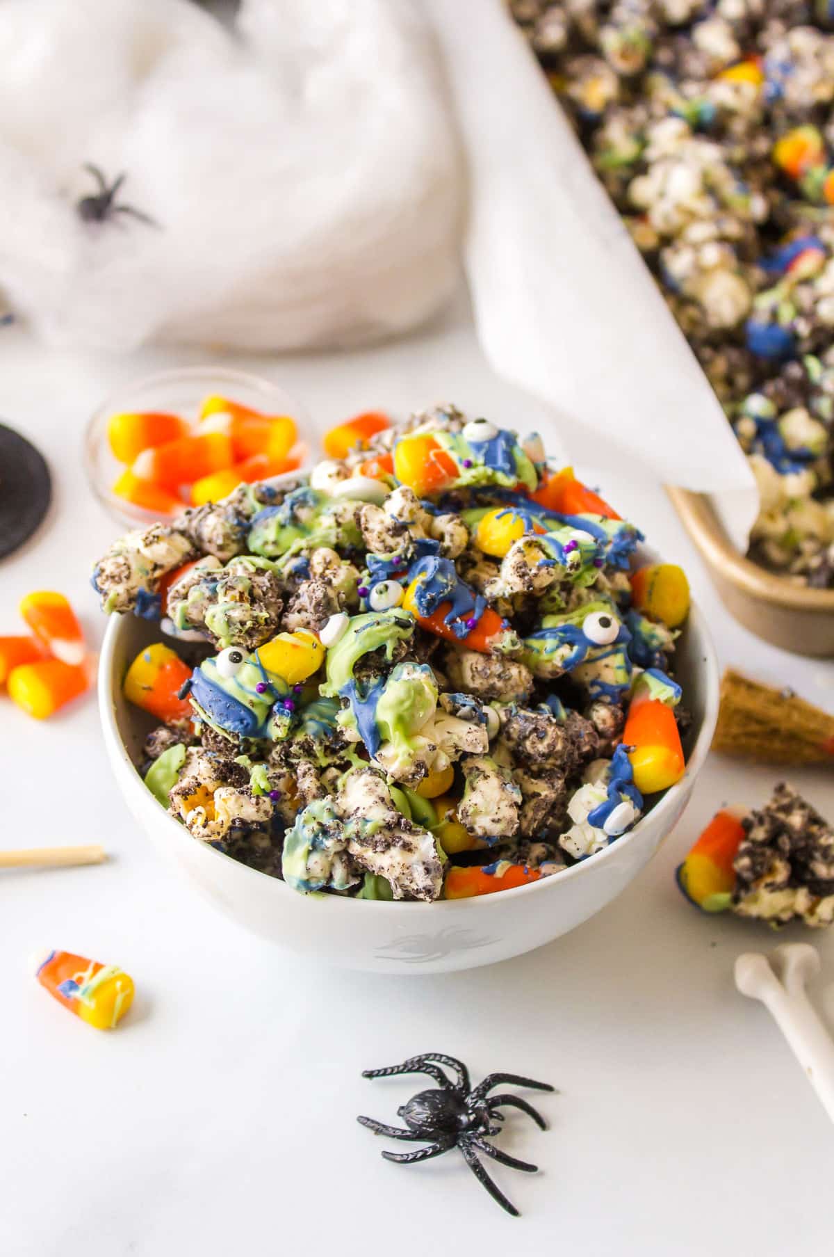 A bowl of Halloween popcorn next to plastic spiders and fake spider webs.