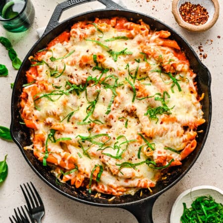A cast iron skillet filled with baked ziti next to black forks.