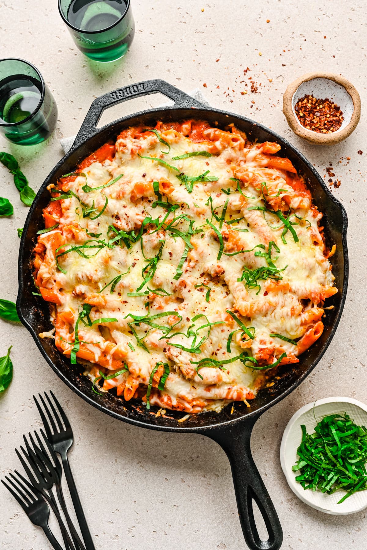 A cast iron skillet filled with baked ziti next to black forks.