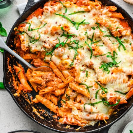 A cast iron skillet filled with baked ziti with a silver spoon scooping up pasta.