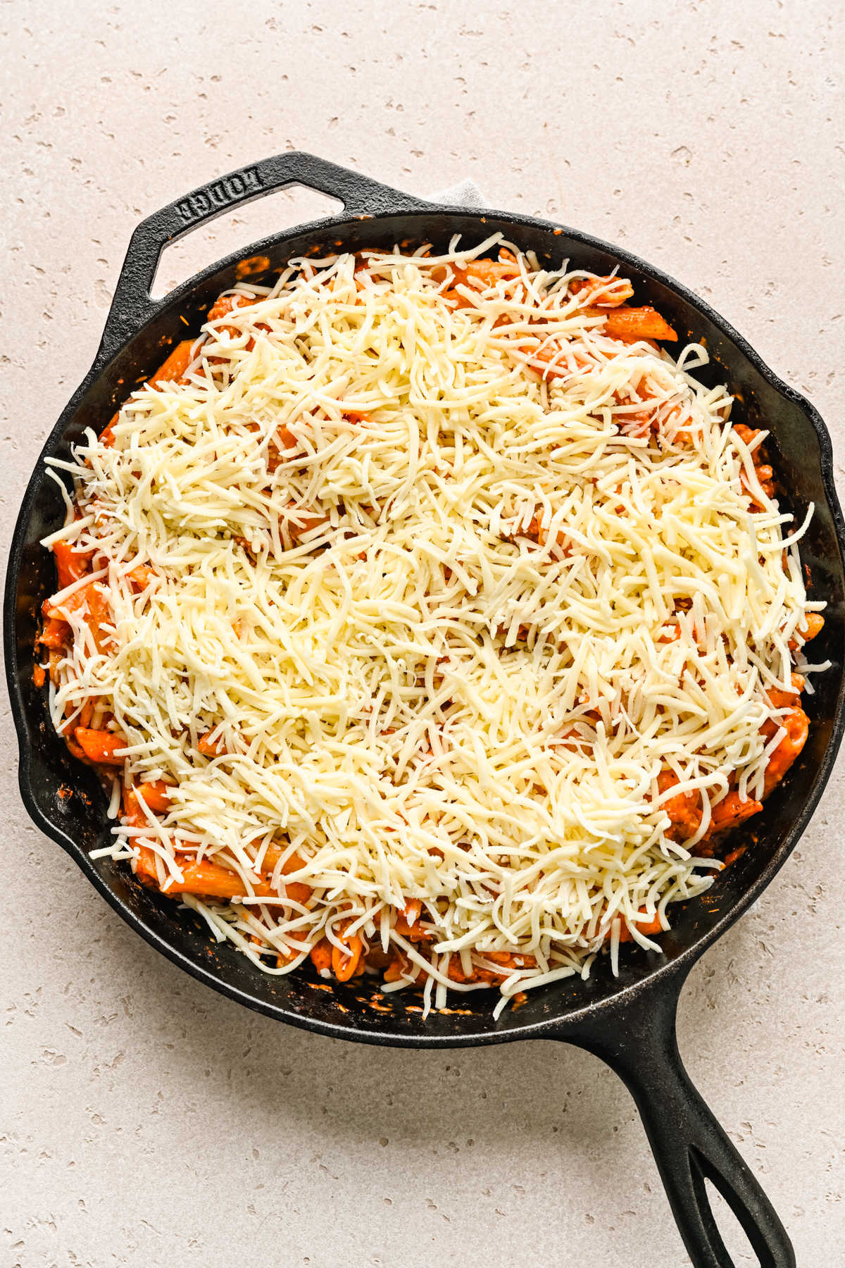 Cooked ziti in a cast iron skillet sprinkled with shredded mozzarella cheese.