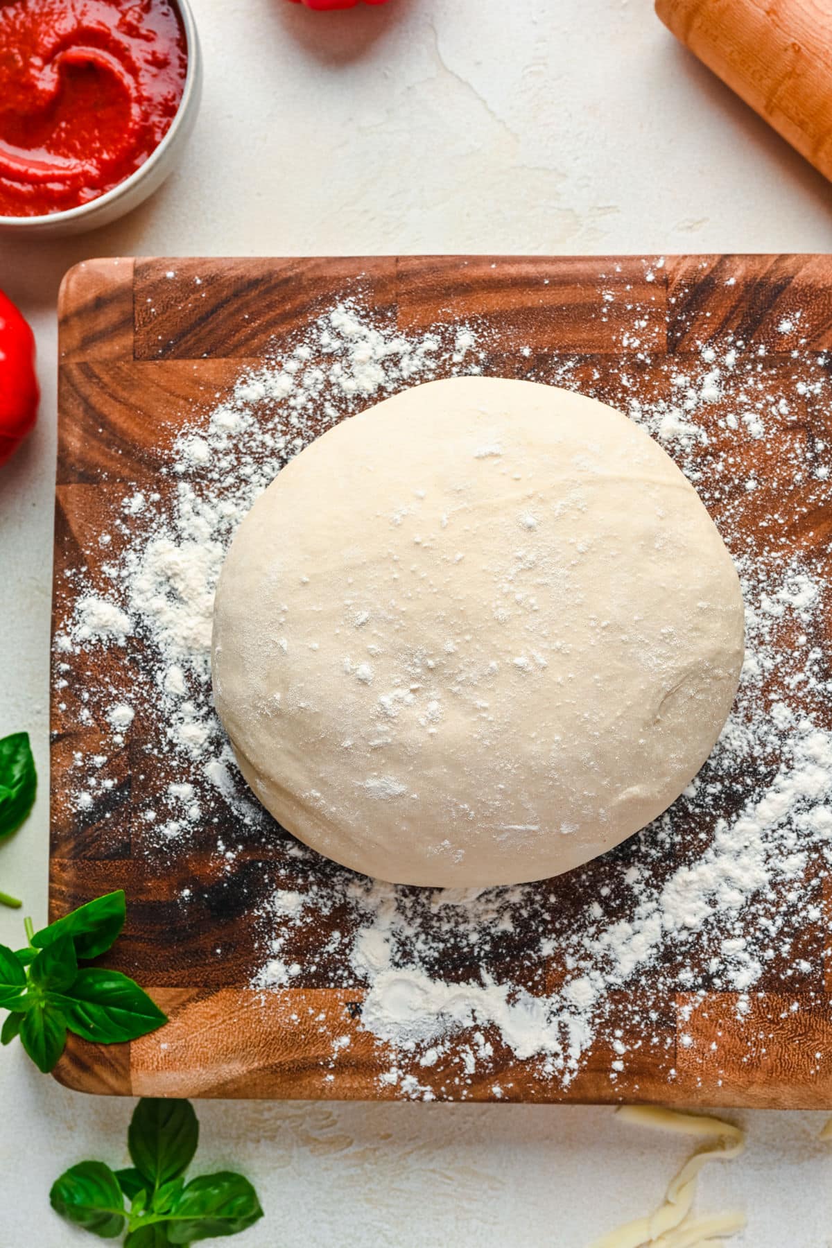 A ball of homemade pizza dough on a wooden cutting board next to a rolling pin.