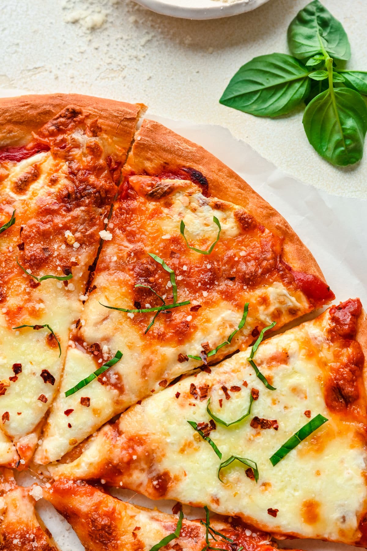 Close up photo of a cheese pizza topped with shredded fresh basil leaves. 