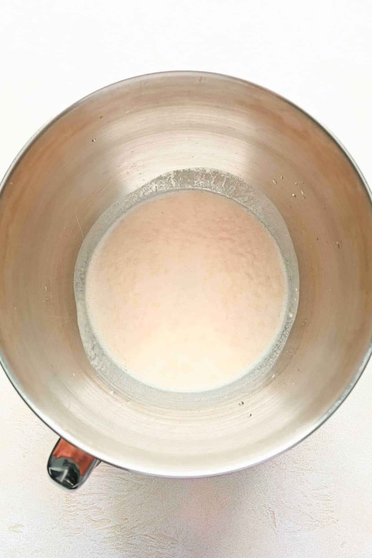 Yeast proofing in warm water in a silver mixing bowl.