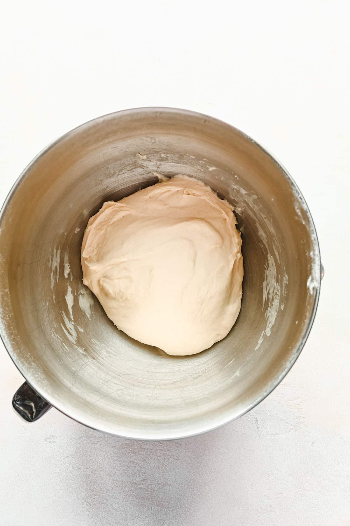 Ball of homemade pizza dough in a silver mixing bowl.