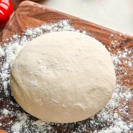 A ball of homemade pizza dough on a floured wooden cutting board.