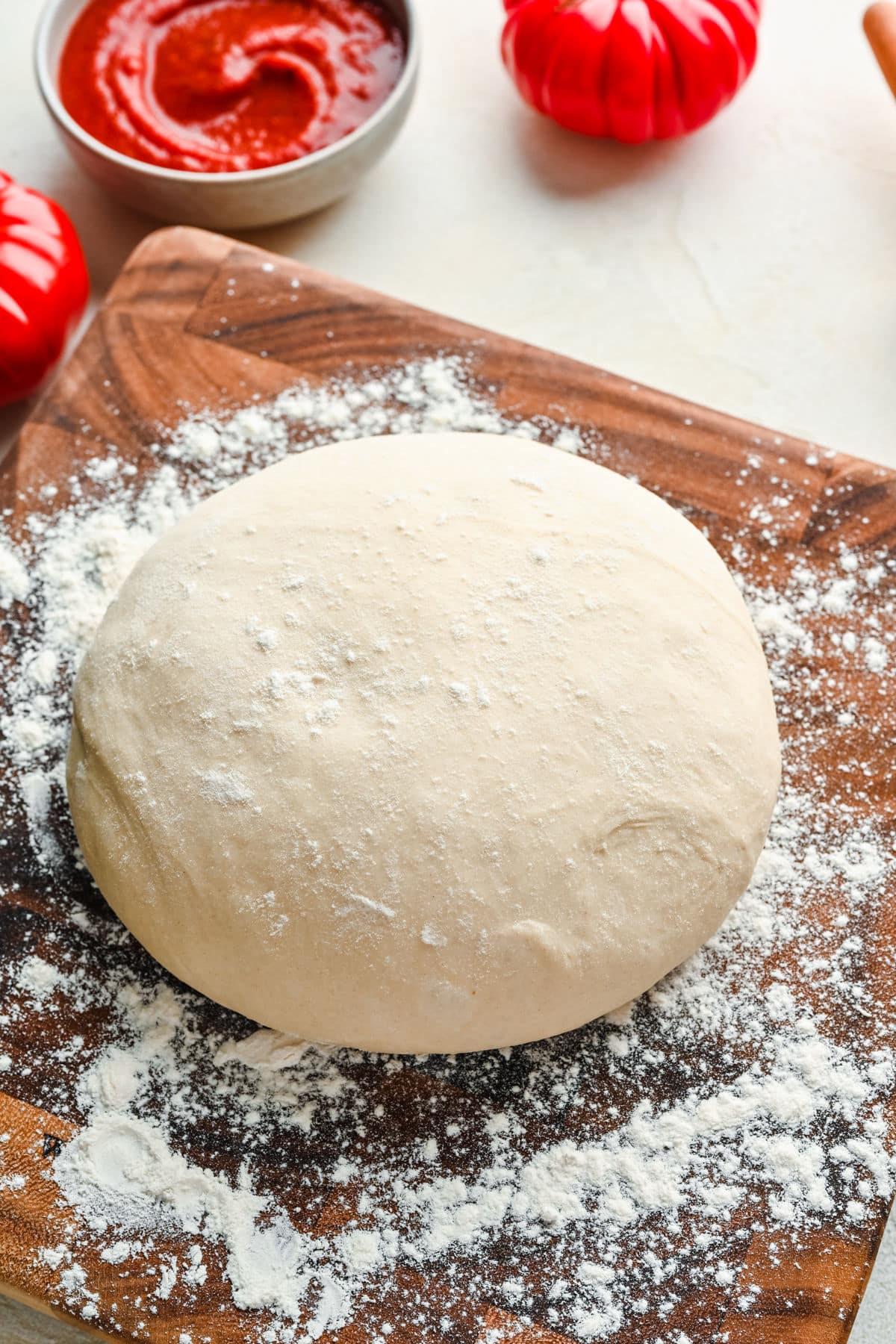 A ball of homemade pizza dough on a floured wooden cutting board.