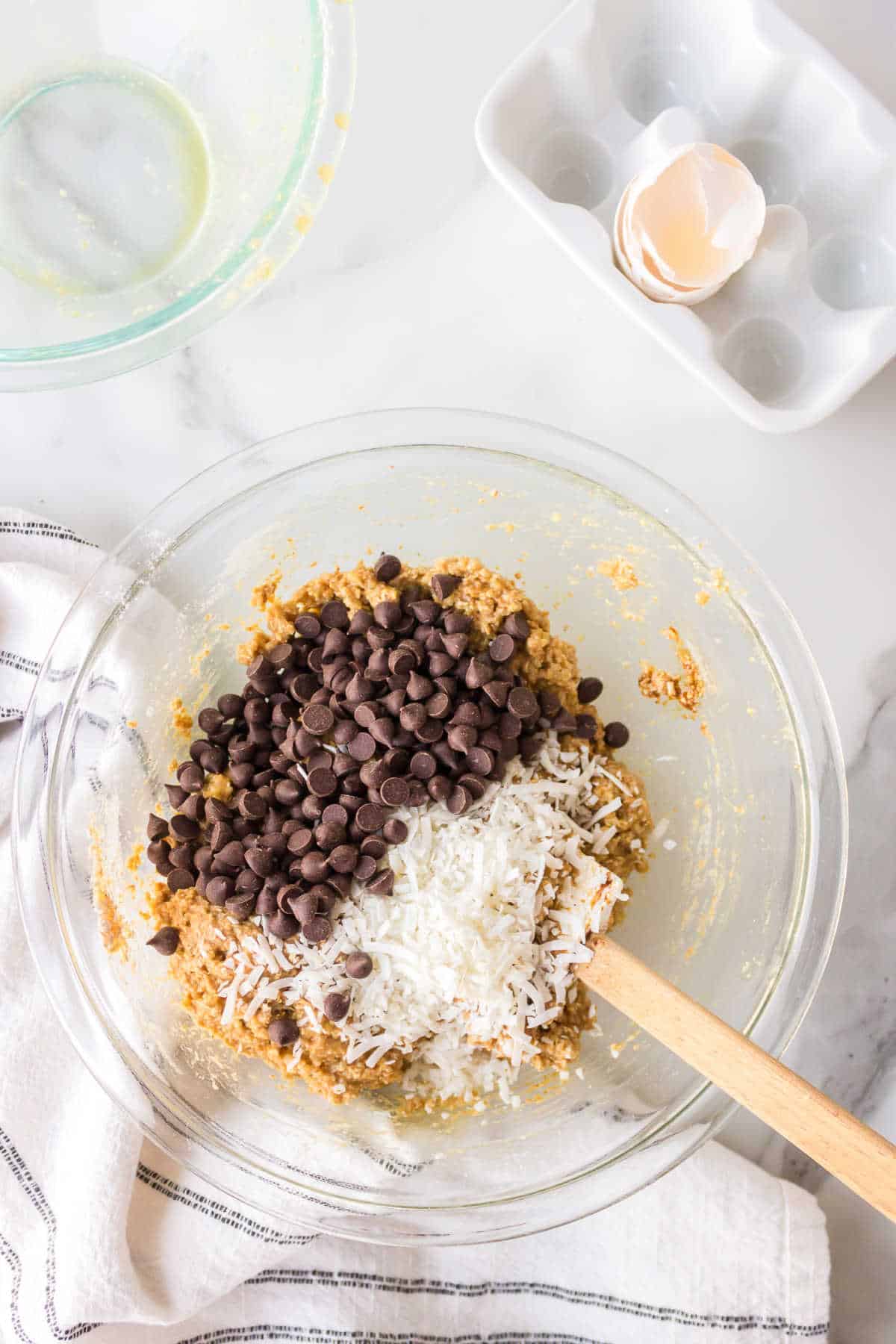 A spatula stirring chocolate chips and dried coconut into quinoa cookie batter. 