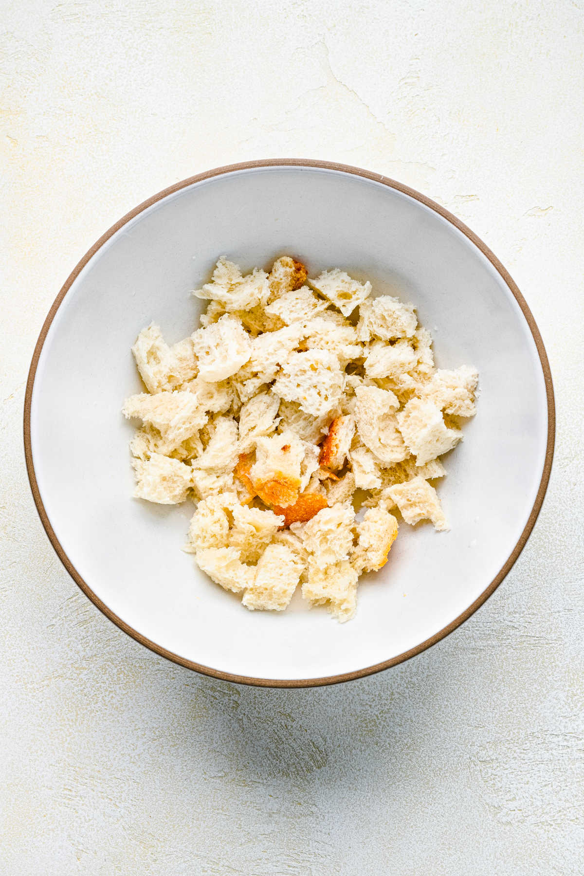 Torn pieces of white bread in milk in a white mixing bowl.