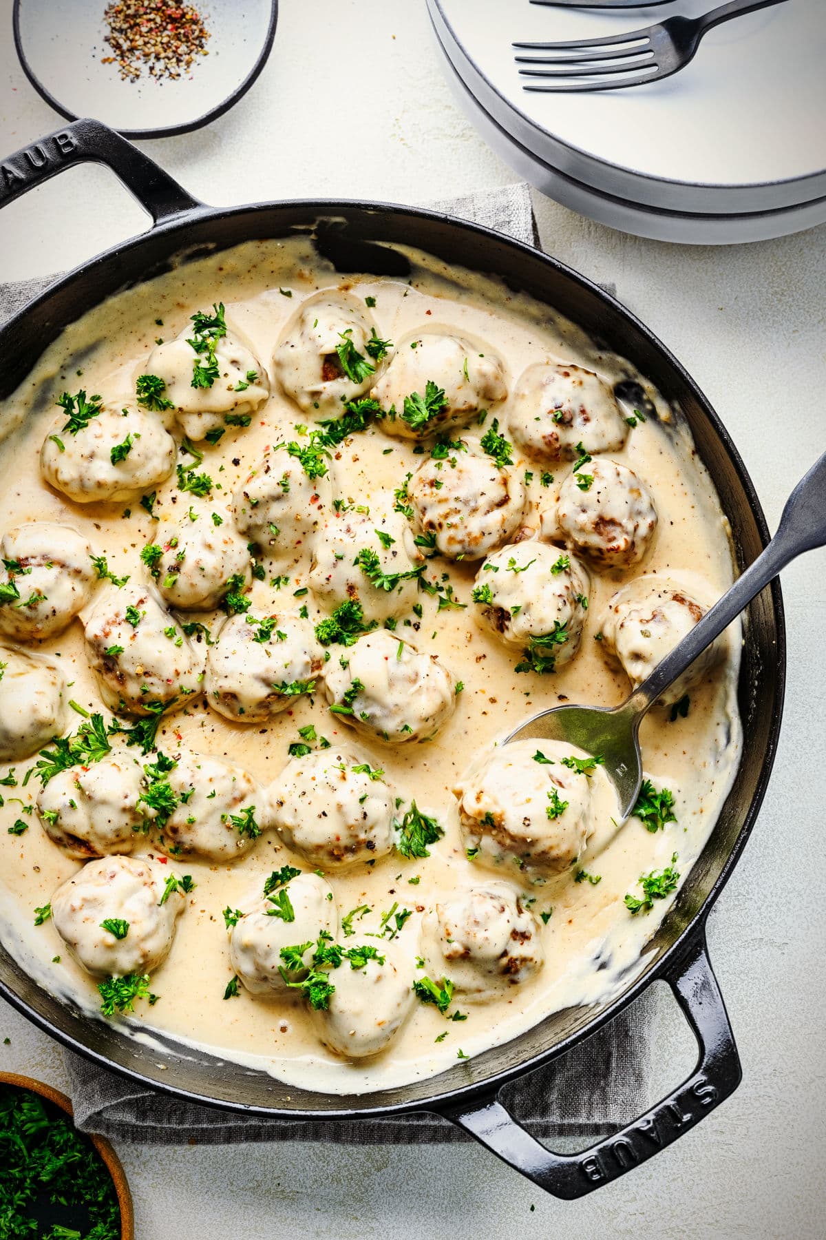 A silver spoon holding a meatball in a cast iron dish of Swedish meatballs.