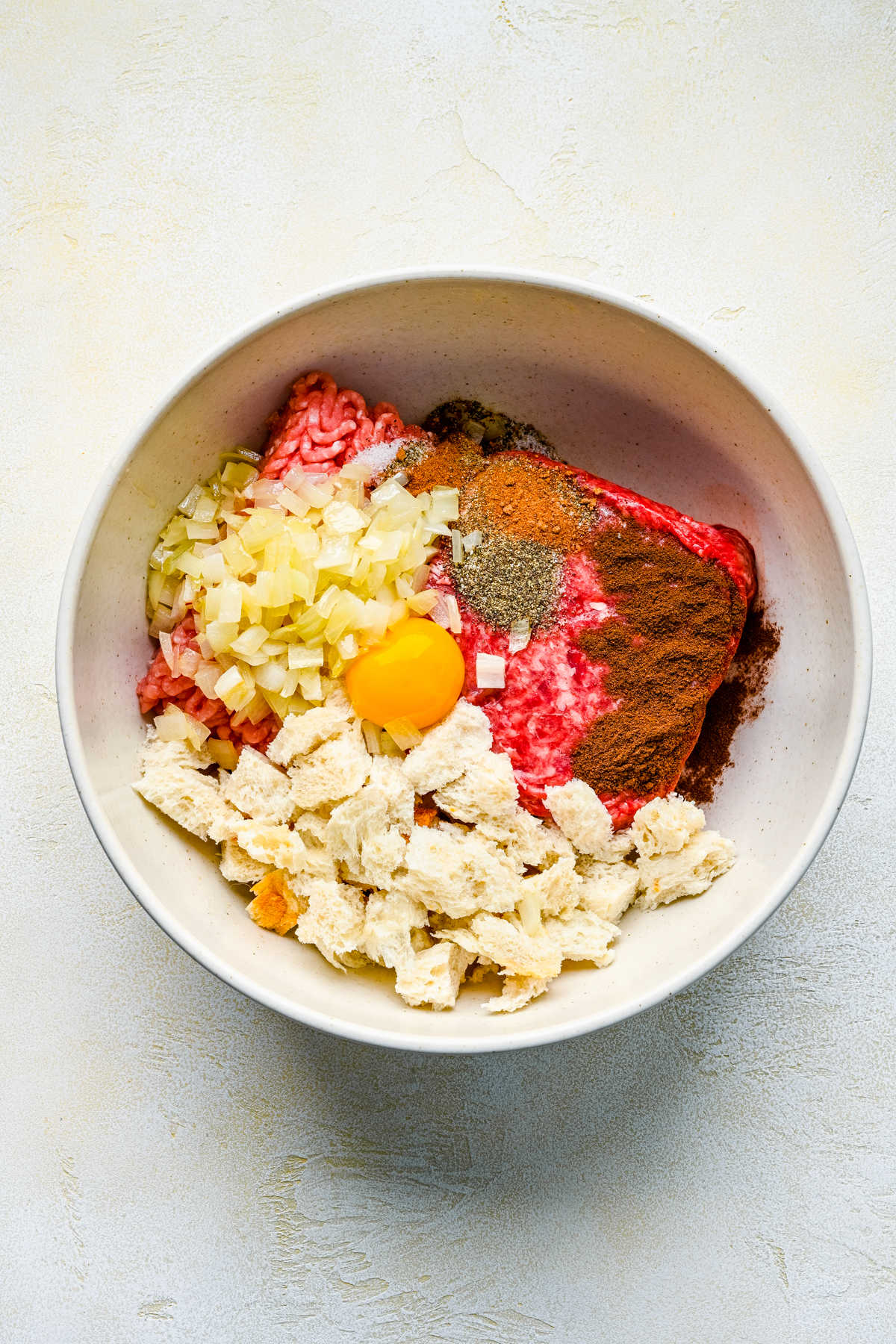 Ground pork seasonings bread and egg in a mixing bowl.
