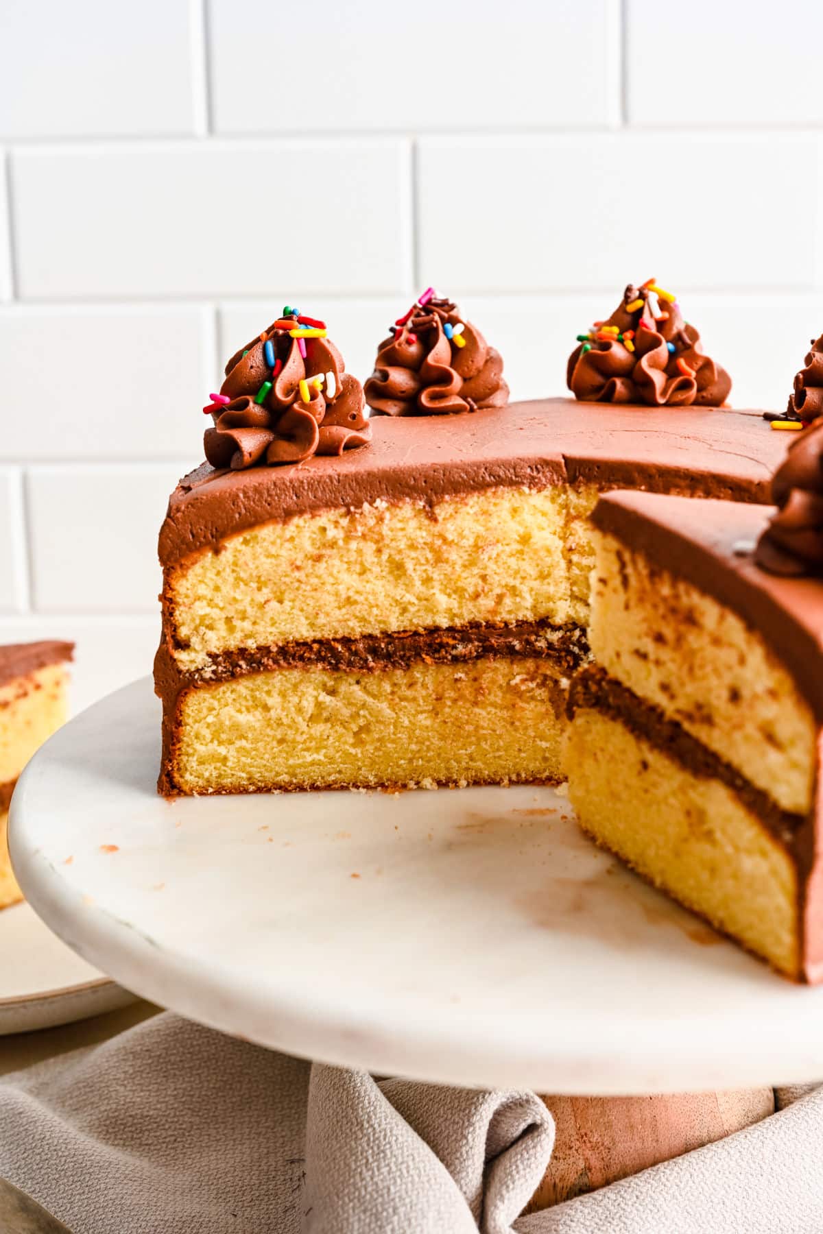 A yellow layer cake with a slice cut from it on a cake stand.