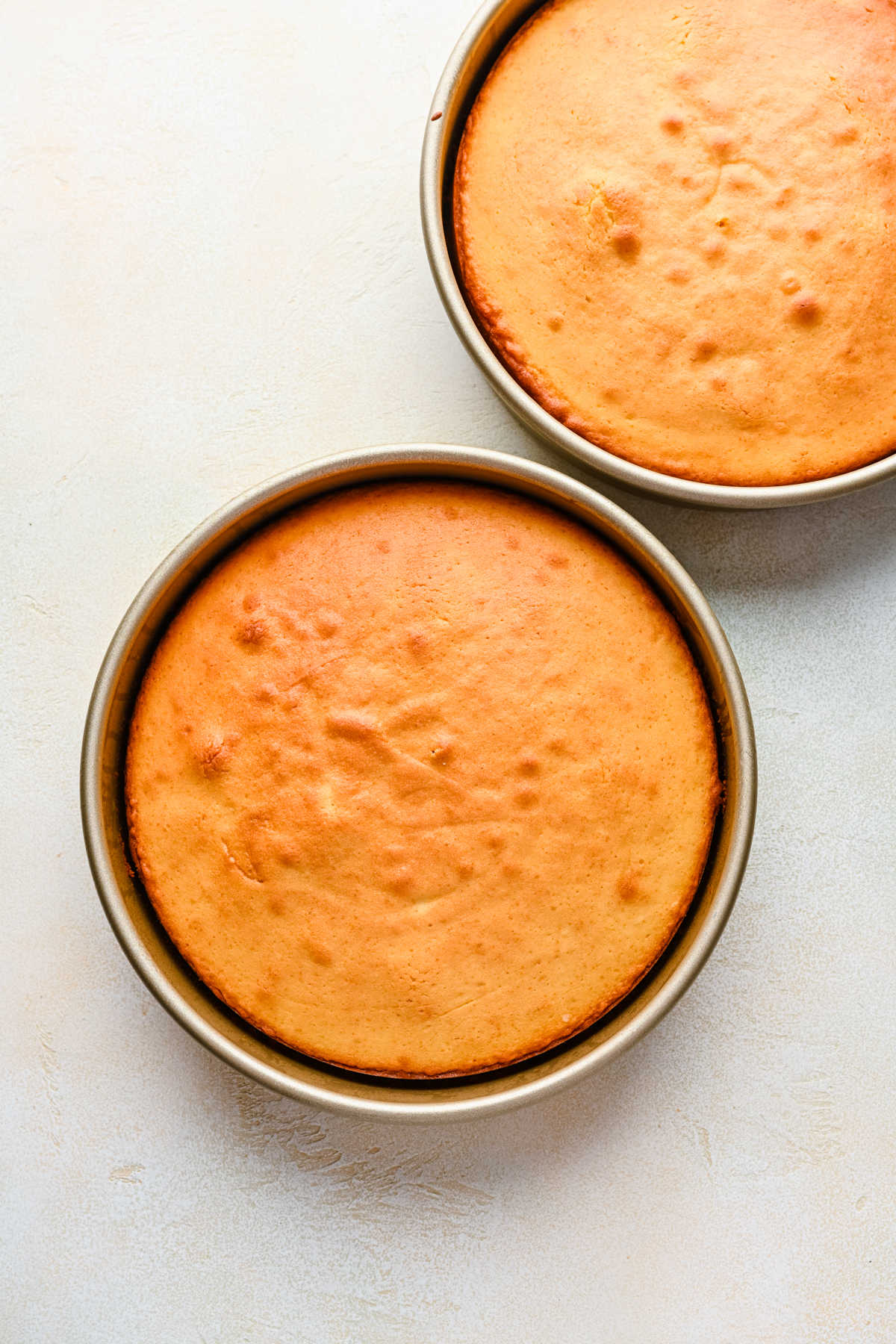 Two baked yellow cakes in round cake pans.