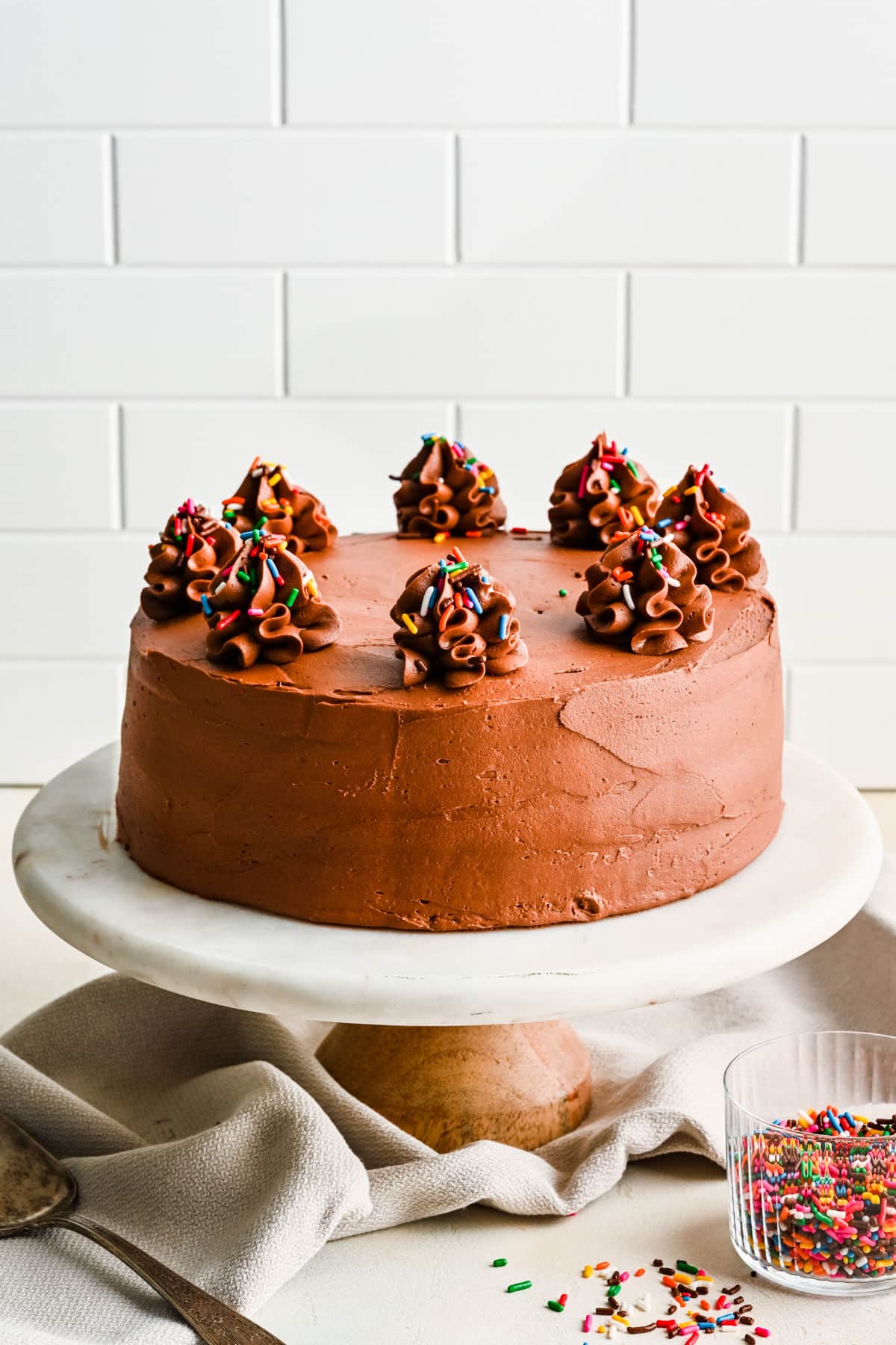 A whole yellow cake frosted with chocolate frosting on a cake stand.