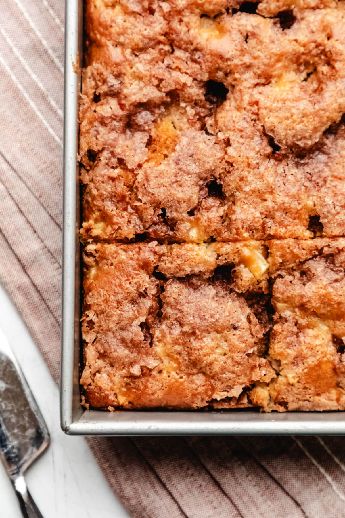 A piece of cake cut in a cinnamon apple cake next to a cake knife. 