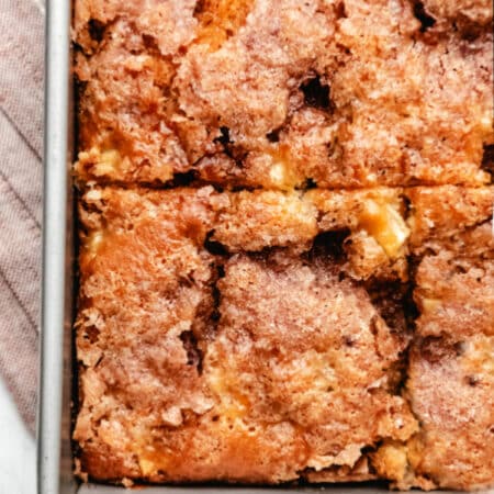 Close up photo of a cut piece of cinnamon apple cake in a metal baking pan.