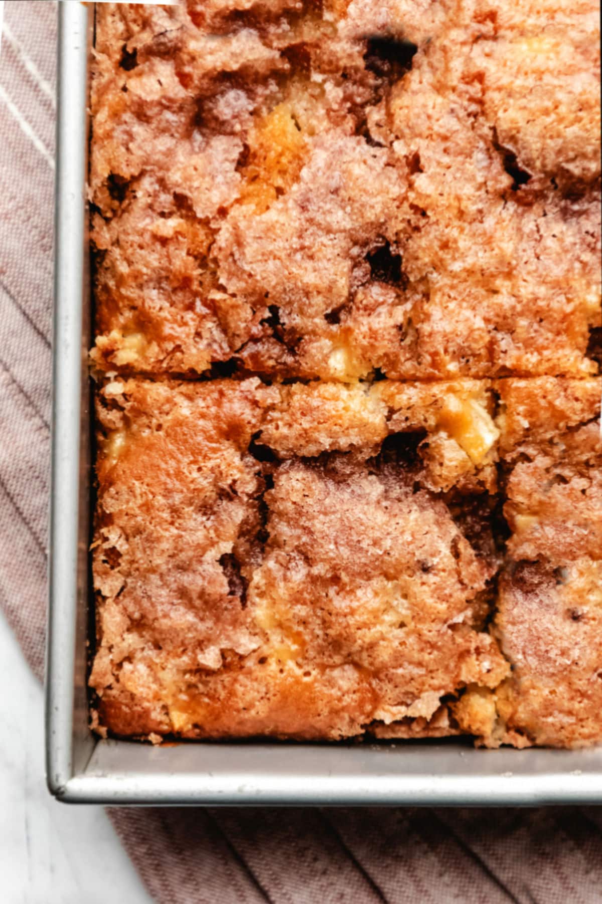 Close up photo of a cut piece of cinnamon apple cake in a metal baking pan.