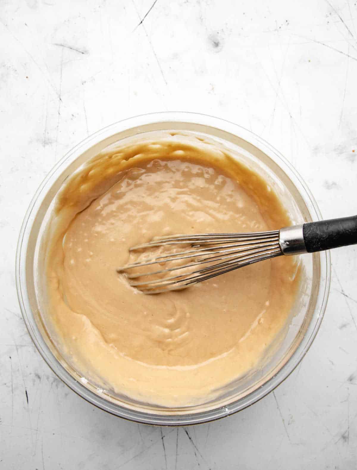 Wet ingredients stirred into dry ingredients in a glass mixing bowl. 