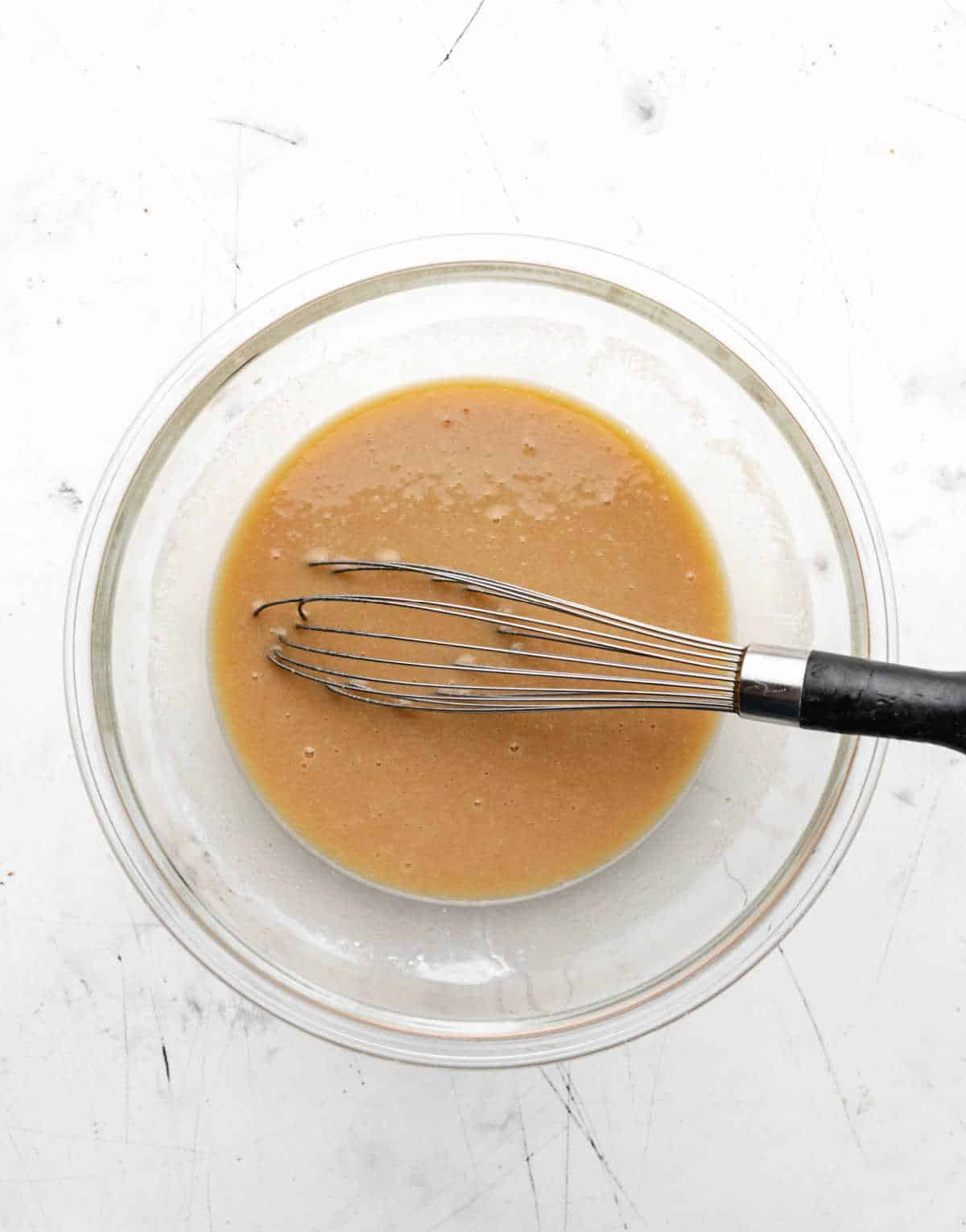 Wet ingredients for apple cake in a glass mixing bowl. 