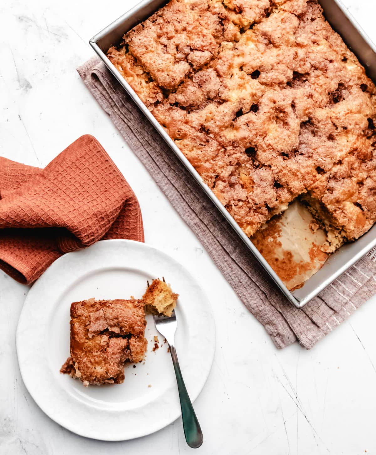 A slice of cinnamon apple cake on a white plate next to the pan of cake. 