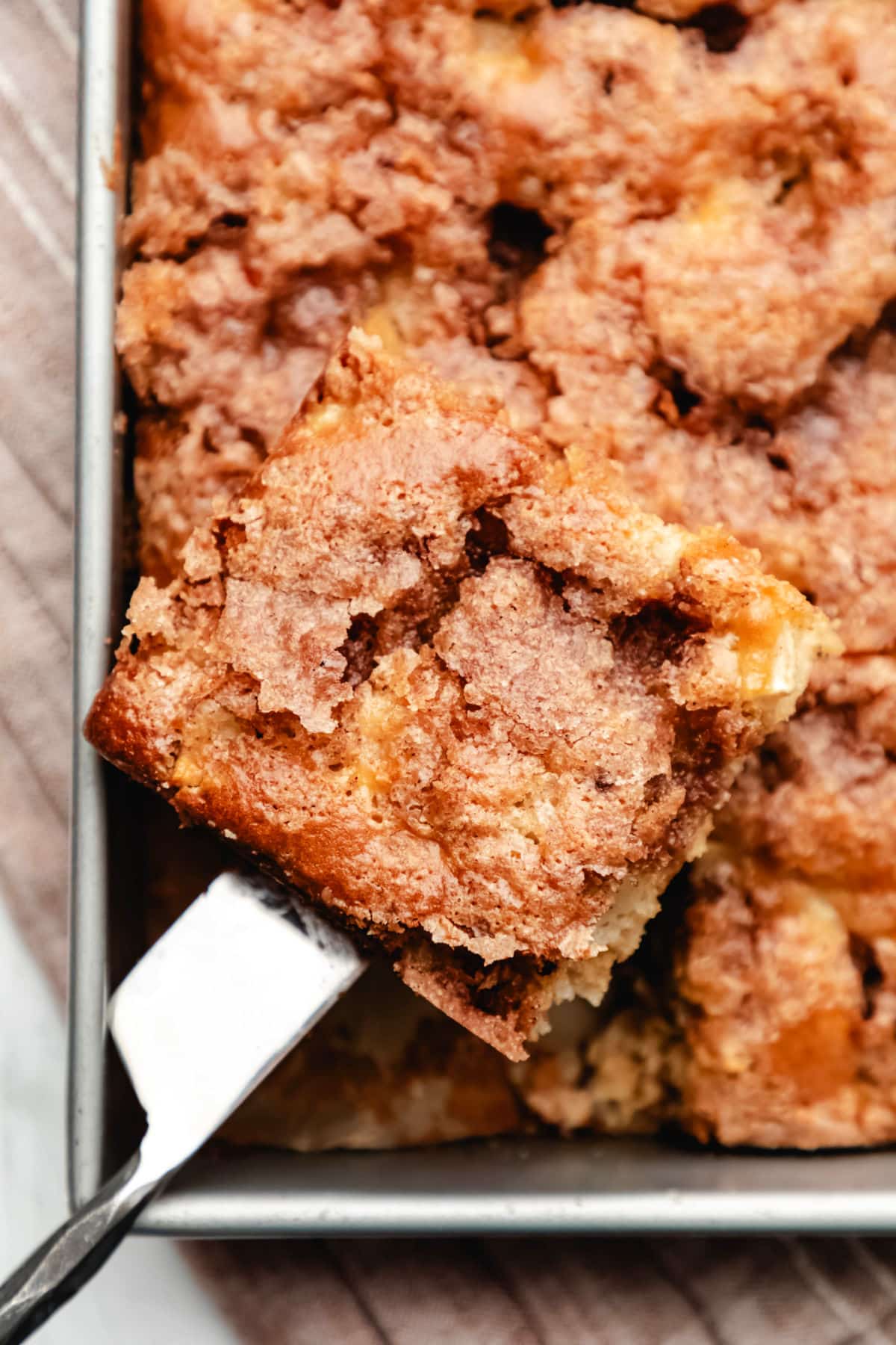 A knife removing a slice of cinnamon apple cake from the pan.