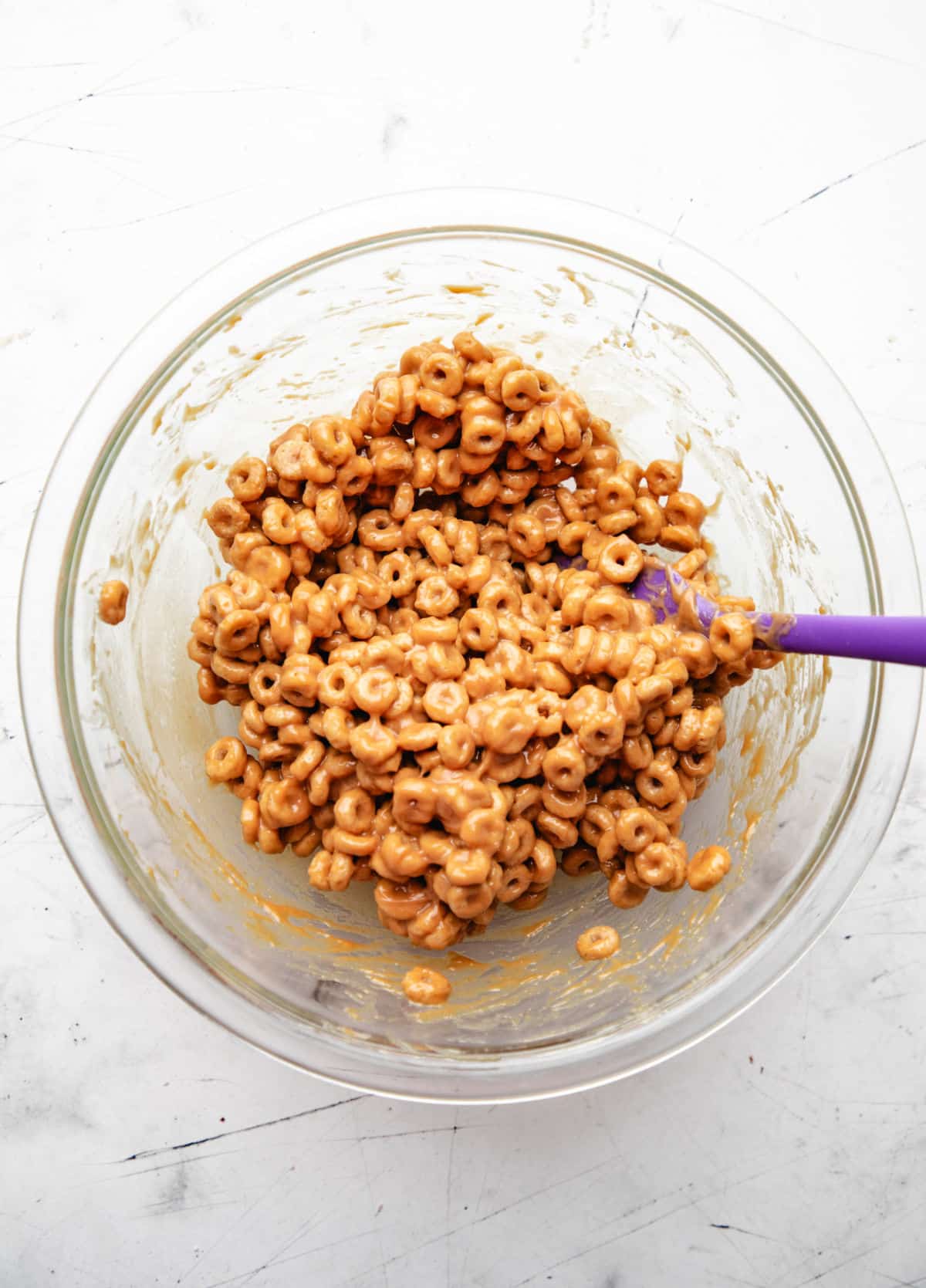 Cheerio cereal coated in honey peanut butter mixture in a glass mixing bowl.