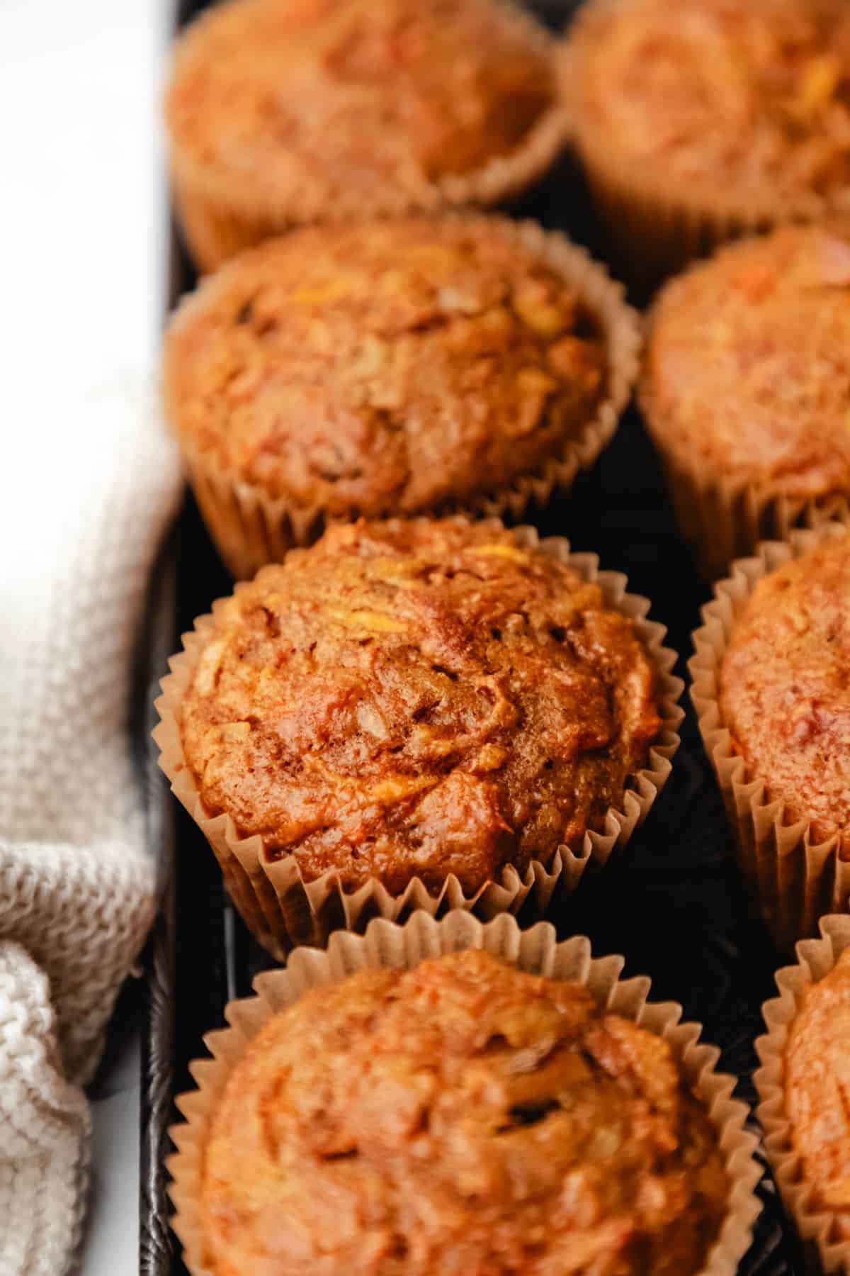 A row of morning glory muffins on a baking tray with a cream knit napkin next to the tray.