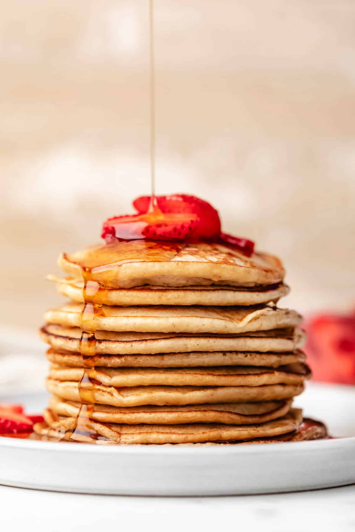 Maple syrup pouring onto a stack of oatmeal pancakes.