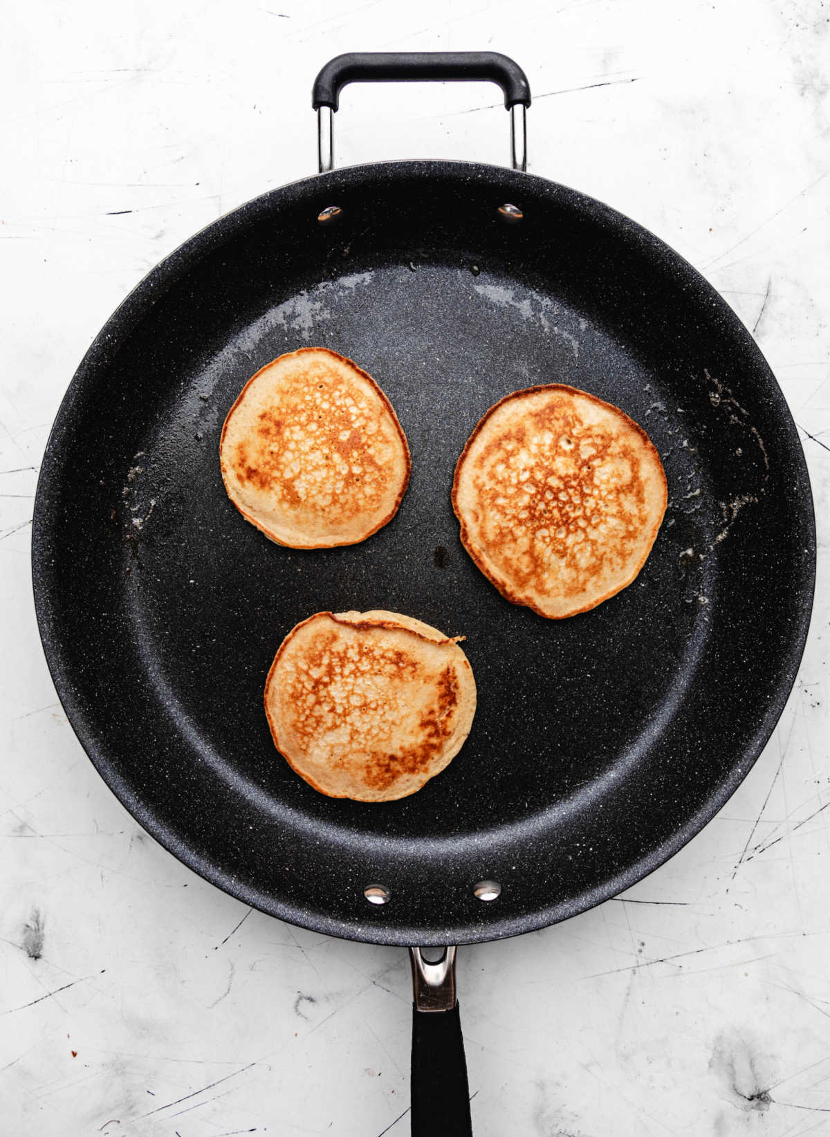 Three cooked oatmeal pancakes in a skillet.