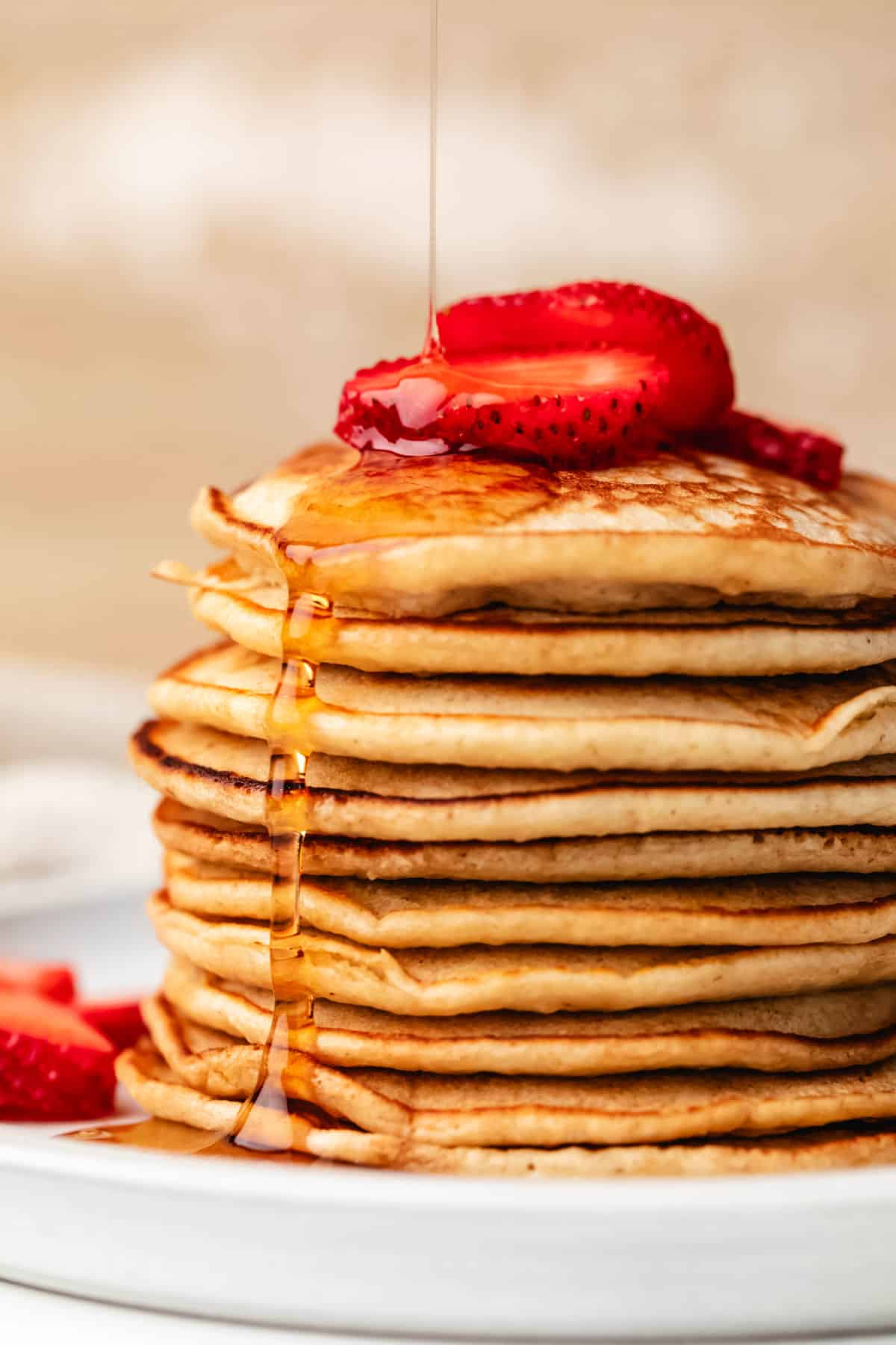 A stack of oatmeal pancakes with maple syrup pouring onto it topped with strawberries.