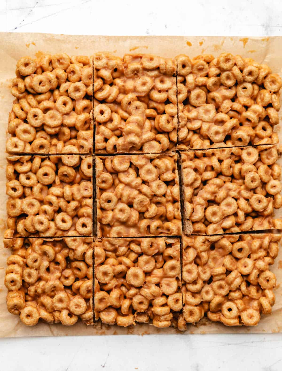 Peanut butter cheerio bars cut into 9 pieces on brown parchment paper. 