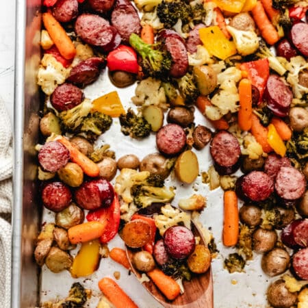 A wooden spoon holding a scoop of sheet pan sausage and veggies.