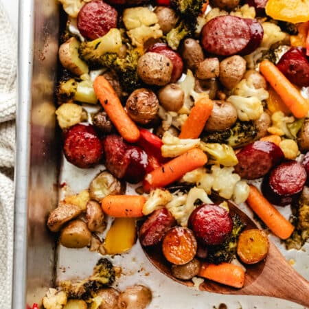 A wooden spoon full of sausage and veggies on a sheet pan.