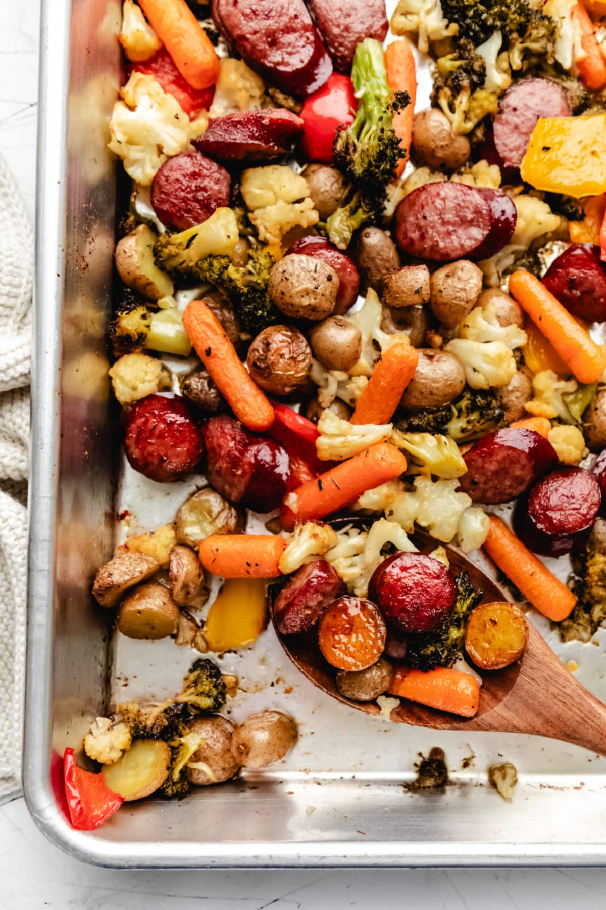 A wooden spoon full of sausage and veggies on a sheet pan.