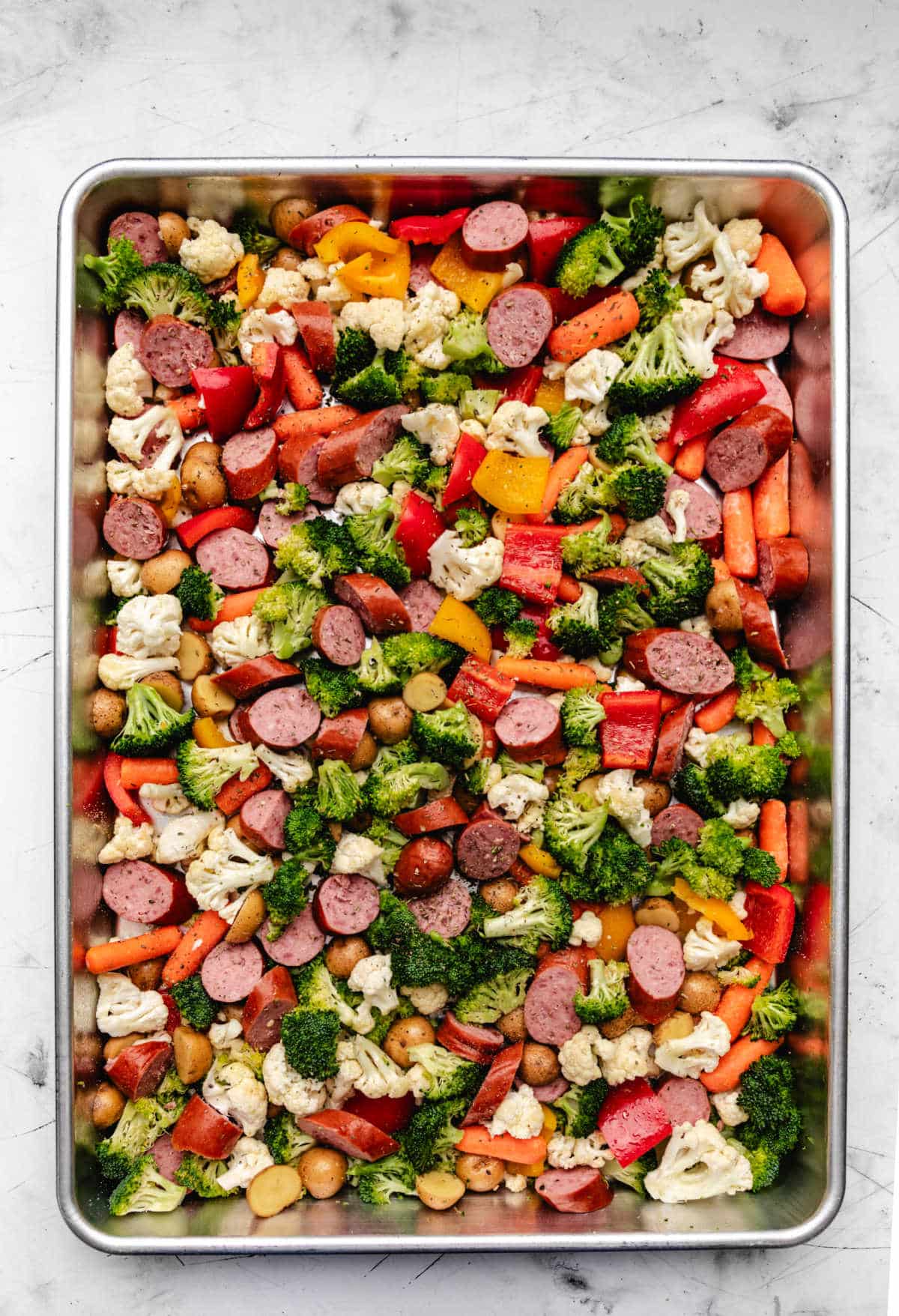 Sheet pan sausage and vegetables sprinkled with seasoning.