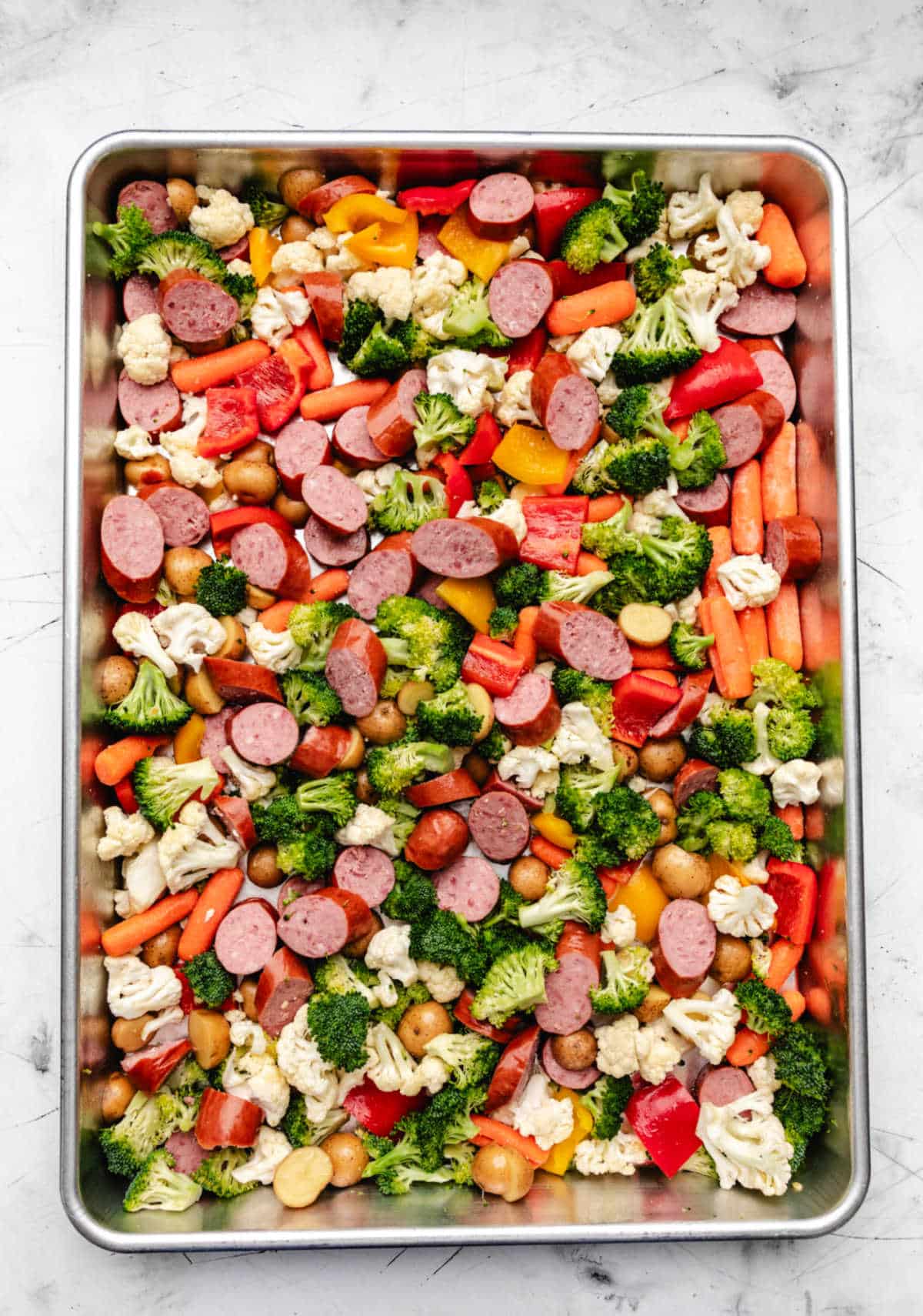 Sheet pan sausage and vegetables drizzled with olive oil.