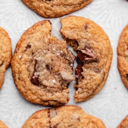 A whole wheat chocolate chip cookie broken in half on white parchment paper.