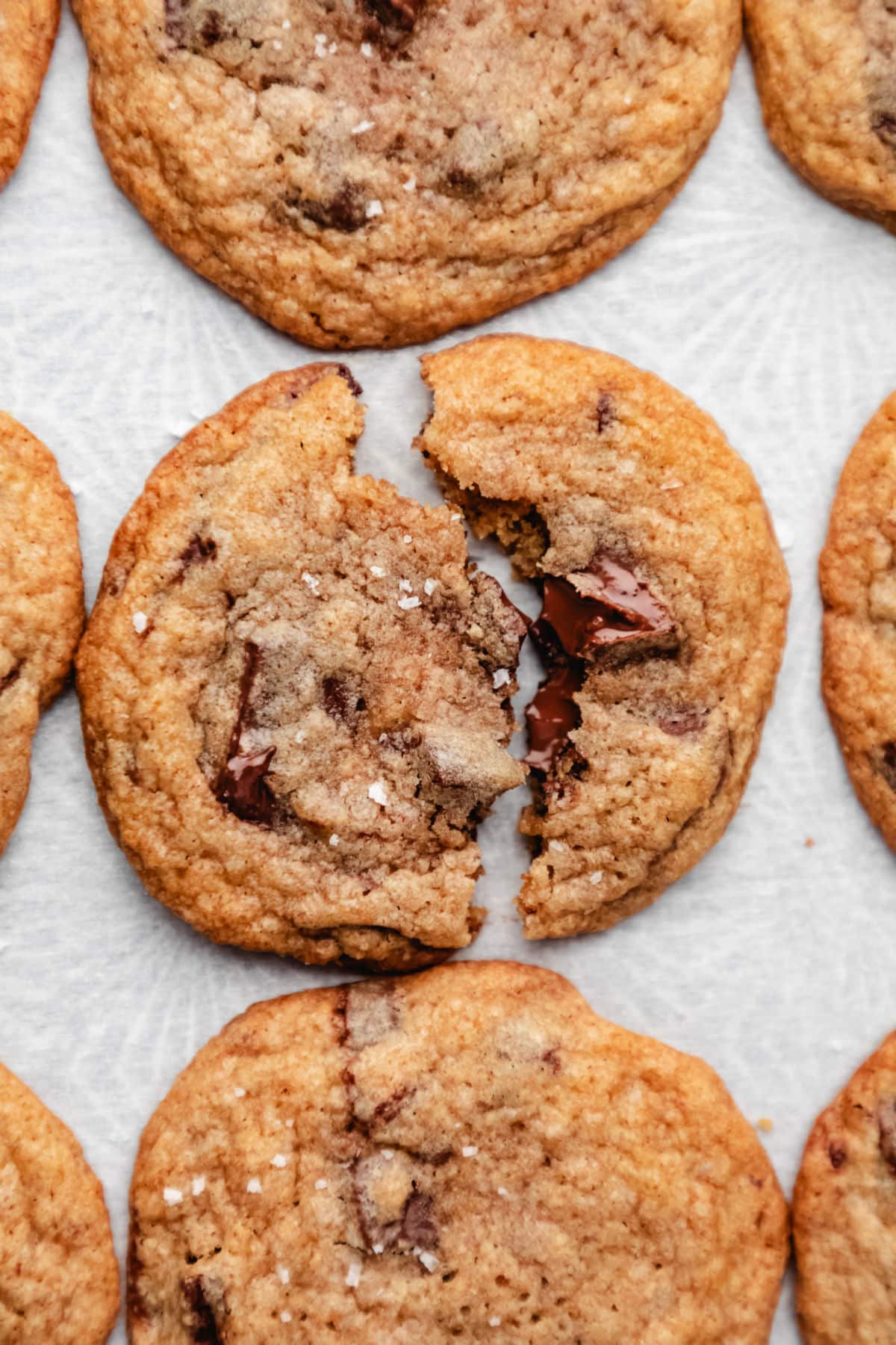 A whole wheat chocolate chip cookie broken in half on white parchment paper. 