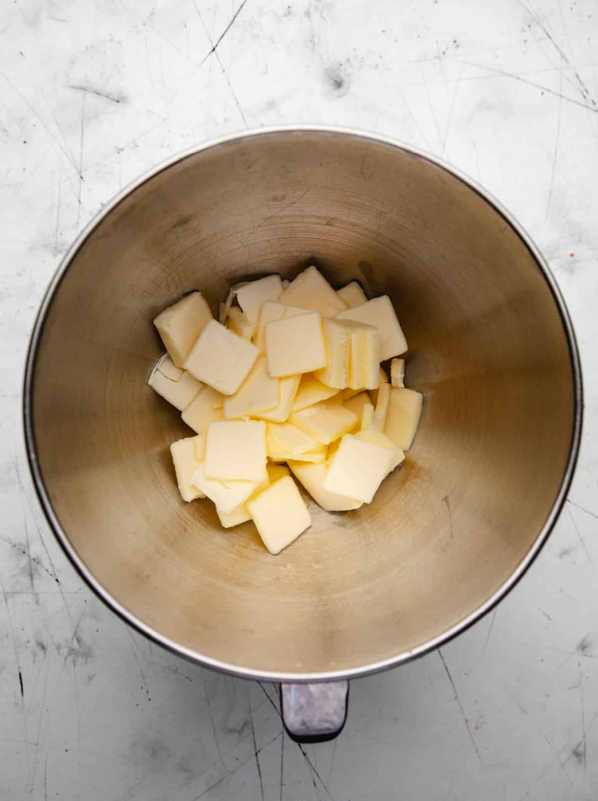 Butter cut into pieces in a silver mixing bowl. 