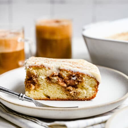 A slice of cinnamon roll poke cake on a white plate with a silver fork.