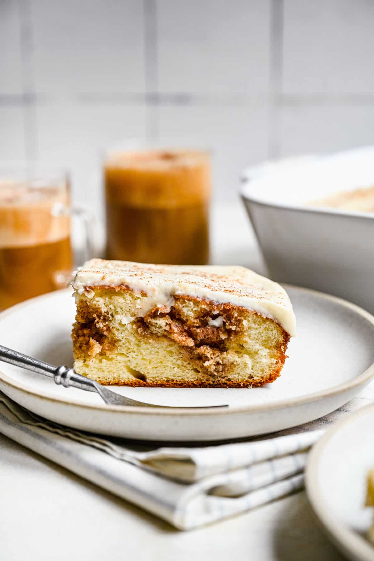 A slice of cinnamon roll poke cake on a white plate with a silver fork. 